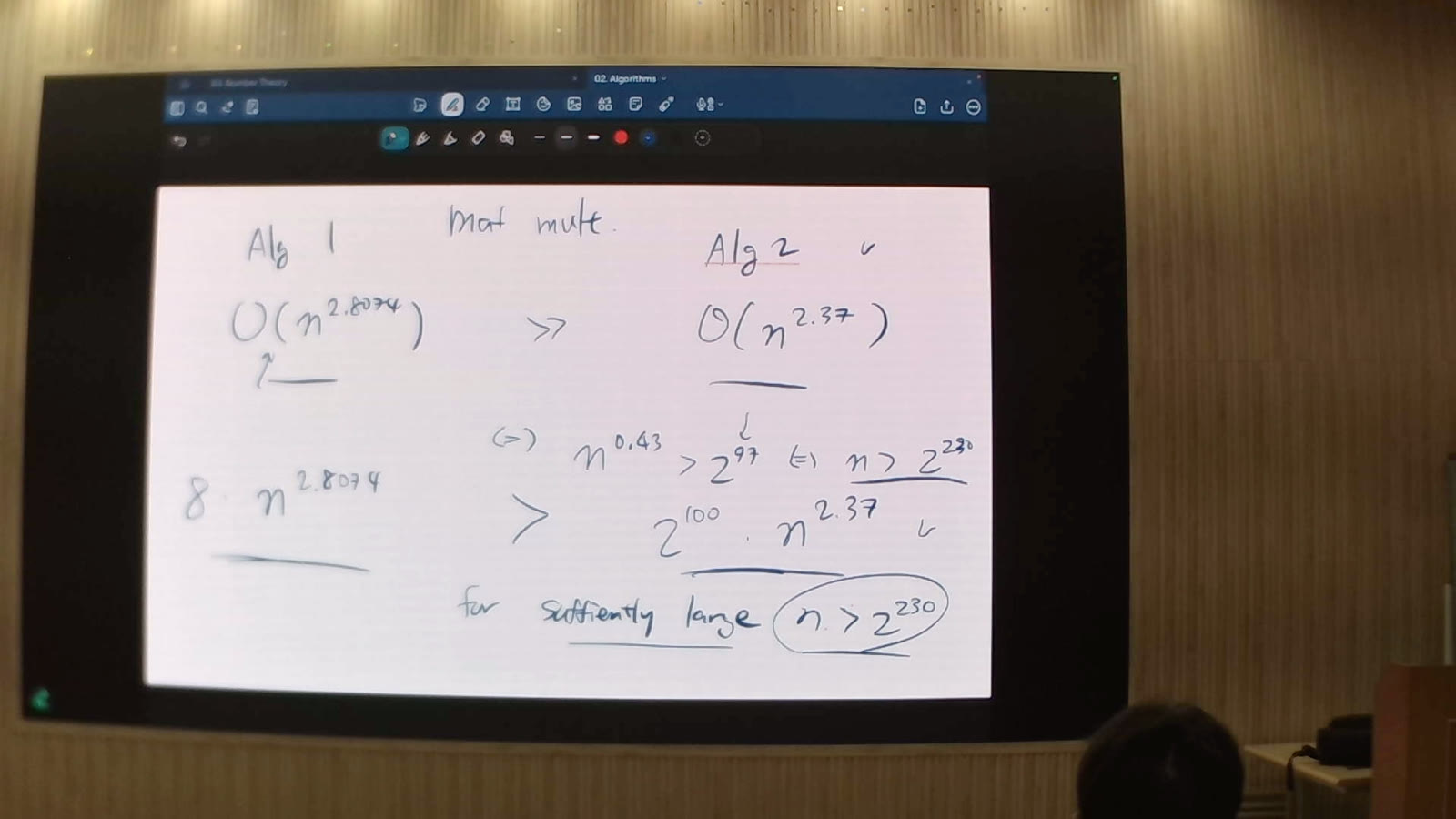 A capture of a lecture screen from the back of the hall: handwritten matrix-multiplication bounds, O(n^2.8074) against O(n^2.37), readable in full