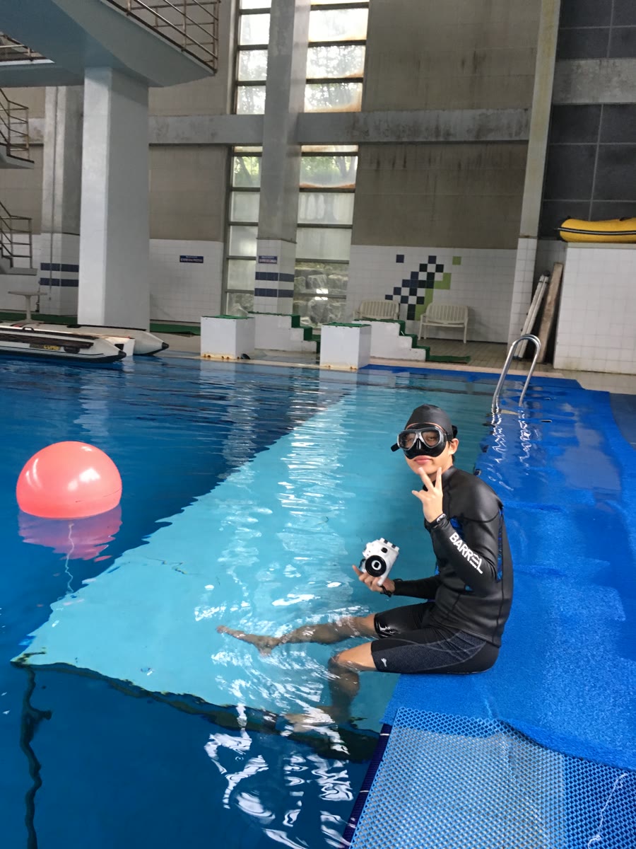 Inkyu in a wetsuit at a dive pool, holding an underwater camera